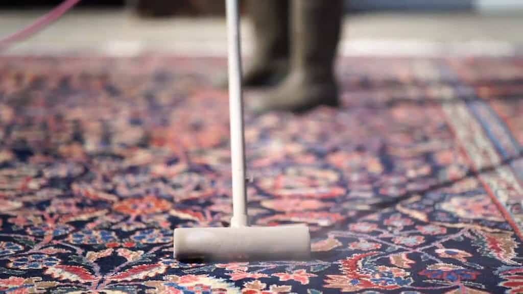 Employee at S&S Rugs, an Atlanta rug cleaning service company, air dusting an oriental rug